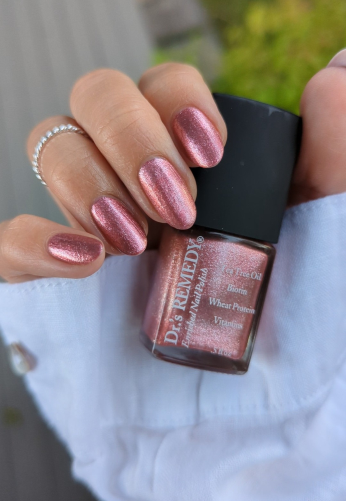 Beautiful nails holding Dr.'s Remedy Enriched Nail Polish in REFLECTIVE Rose, a frosted metallic pink shade with flecks of shimmery chrome, enriched with Tea Tree Oil, Biotin, and Wheat Protein for healthy nails