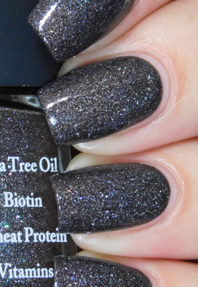 Beautiful nails holding Dr.'s Remedy Enriched Nail Polish in MAGNETIC Midnight, an intergalactic charcoal with glittery specks of mulitcolour shimmer, enriched with Tea Tree Oil, Biotin, and Wheat Protein for healthy nails