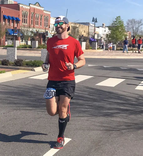 Man running marathon wearing OS1st FS4+ Compression Bracing Socks in black, providing targeted support for Plantar Fasciitis, foot pain relief, and improved recovery with compression technology.