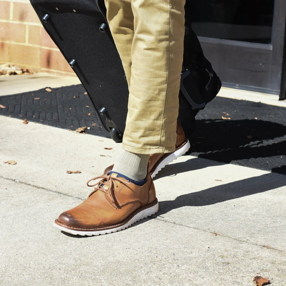 Man walking with suitcase wearing OS1st TS5 Travel Socks in tan, providing compression support to improve circulation and reduce discomfort during travel and long periods of sitting.
