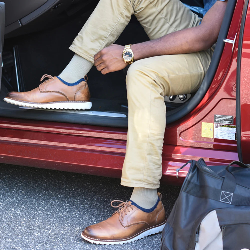 Man sitting in car with door open wearing OS1st TS5 Travel Socks in tan, providing compression support to improve circulation and reduce discomfort during travel and long periods of sitting.