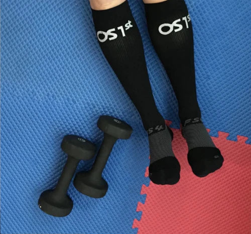 Legs on exercise mat next to dumbells waering OS1st FS4 Compression Bracing Socks in black, providing targeted support for Plantar Fasciitis, foot pain relief, and improved recovery with compression technology.