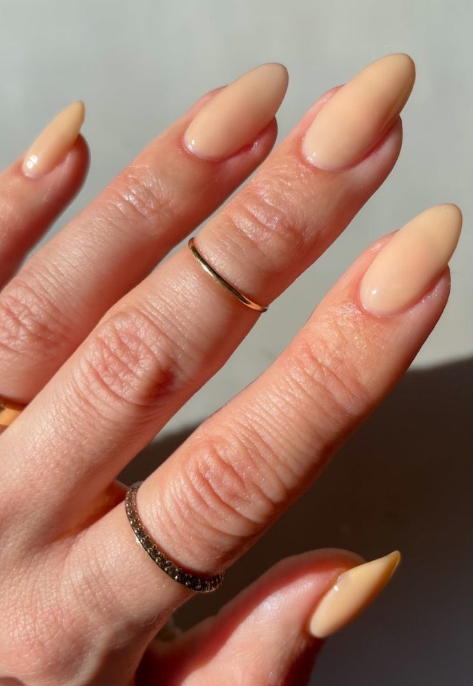 Beautiful nails painted with Dr.'s Remedy Enriched Nail Polish in PURITY Peach, a classic ultra sheer nude with peachy-pink hues, showcasing a glossy finish and complemented by gold rings