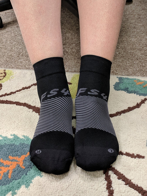 Ladies lower leg wearing black OS1st FS4 Quarter Crew Socks designed for Plantar Fasciitis relief, providing targeted compression and support for the arch and heel of the foot.