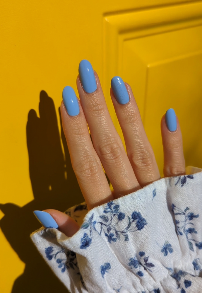 Beautiful nails painted with Dr.'s Remedy Enriched Nail Polish in PERCEPTIVE Periwinkle, a pastel blue with soft lavender hue and a barely there shimmer, showcasing a glossy finish against a yellow background
